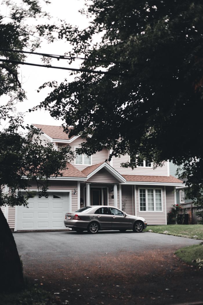 A modern suburban house with a parked car on the driveway surrounded by trees.